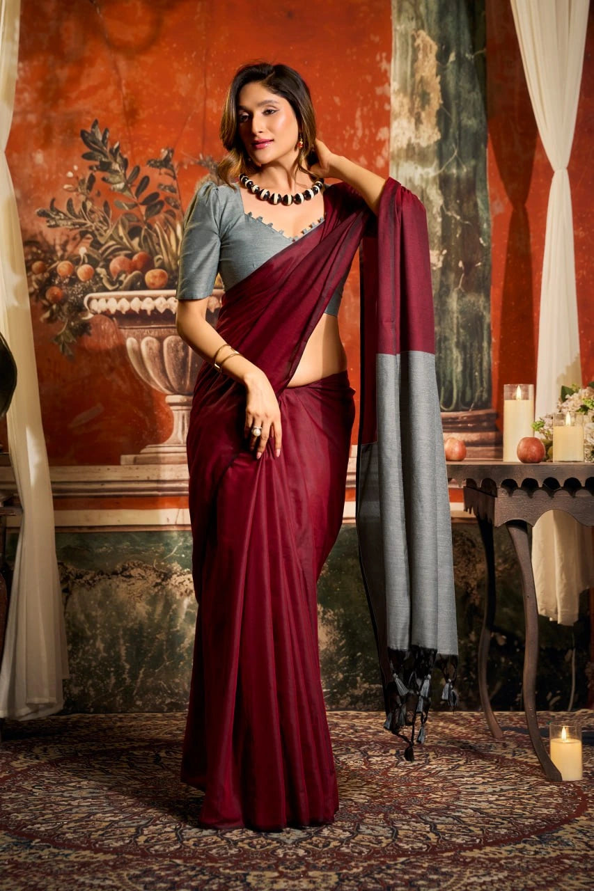 Woman in a maroon saree with a gray blouse in an ornate room.