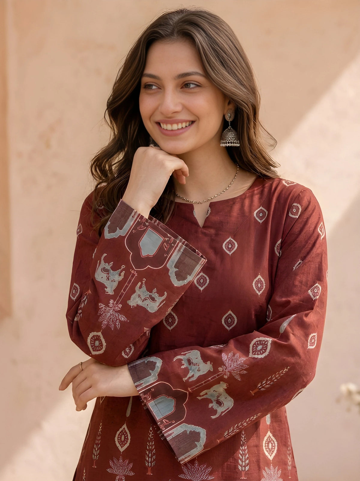 Woman wearing a maroon patterned dress holding a matching clutch against a beige wall.