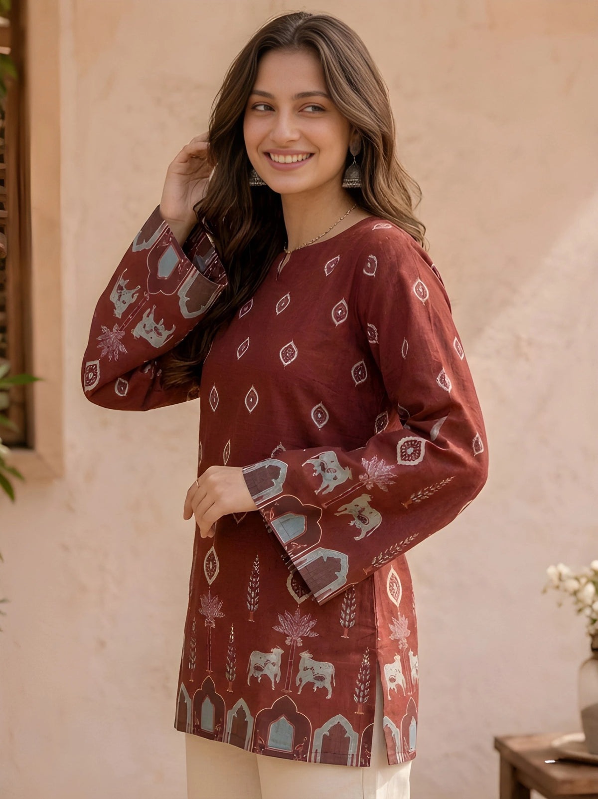 Woman wearing a patterned maroon top against a beige wall.
