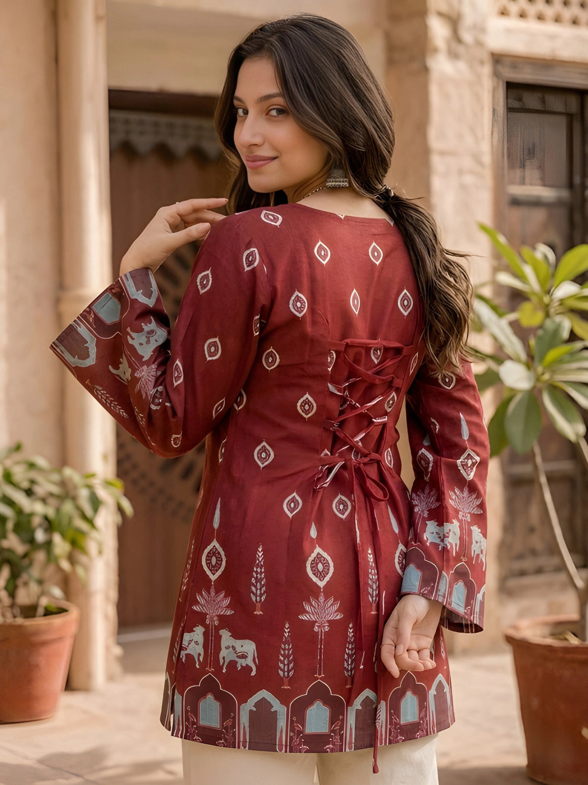Woman wearing a red patterned dress standing outdoors with plants in the background