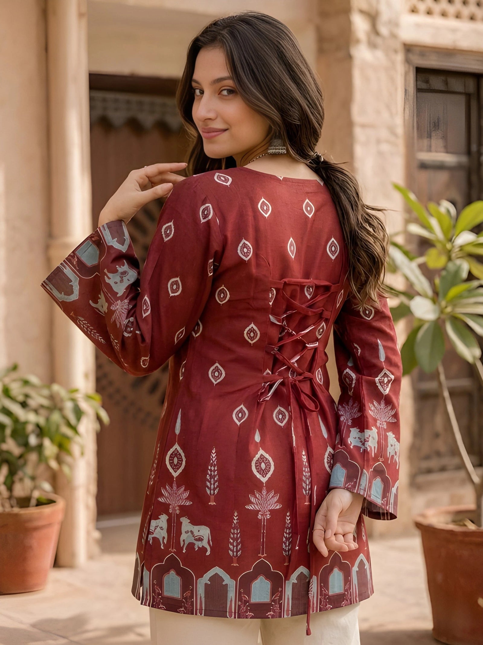 Woman wearing a red patterned dress standing outdoors with plants in the background