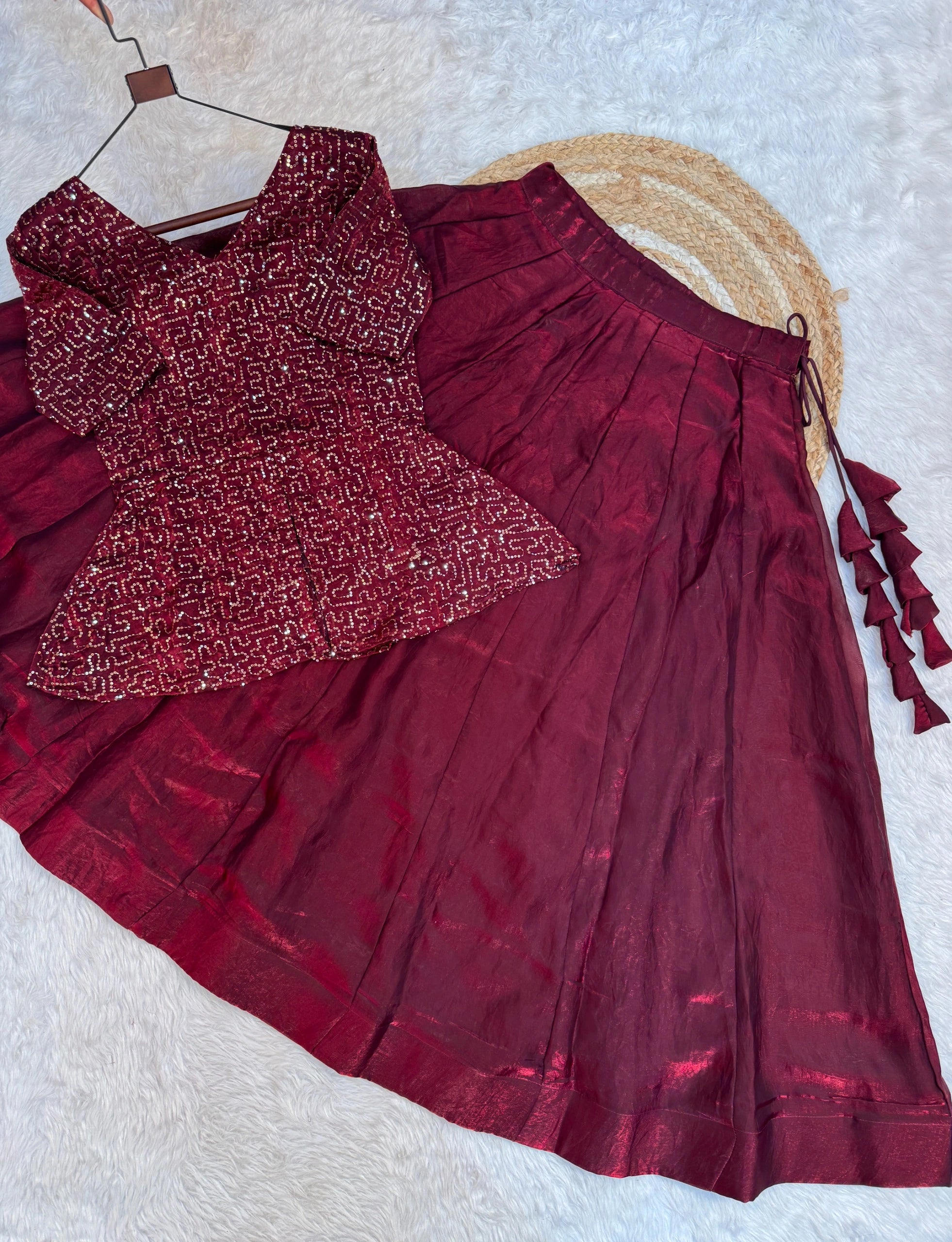 Maroon traditional outfit with a patterned top and pleated skirt on a textured surface