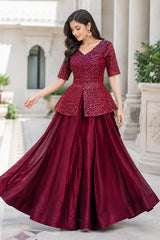 Woman wearing a maroon traditional outfit with a peplum top and long skirt in front of classical architecture.