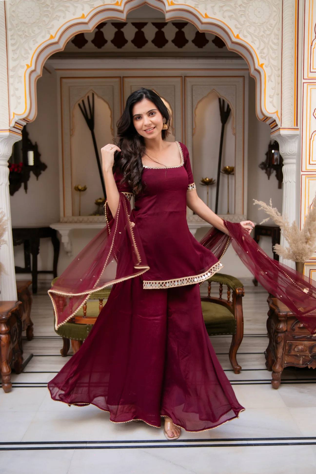 Woman in a maroon traditional outfit standing in an ornate room.