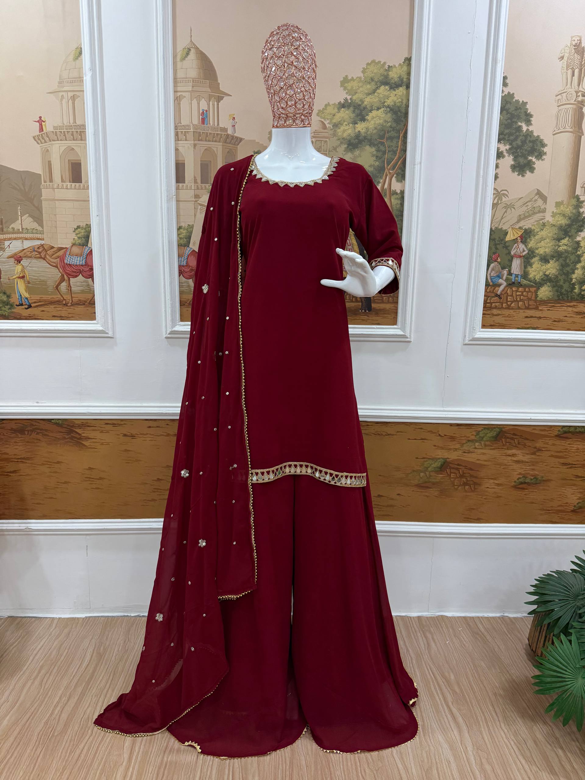 Maroon traditional outfit with a dupatta on a mannequin against a decorative wall.