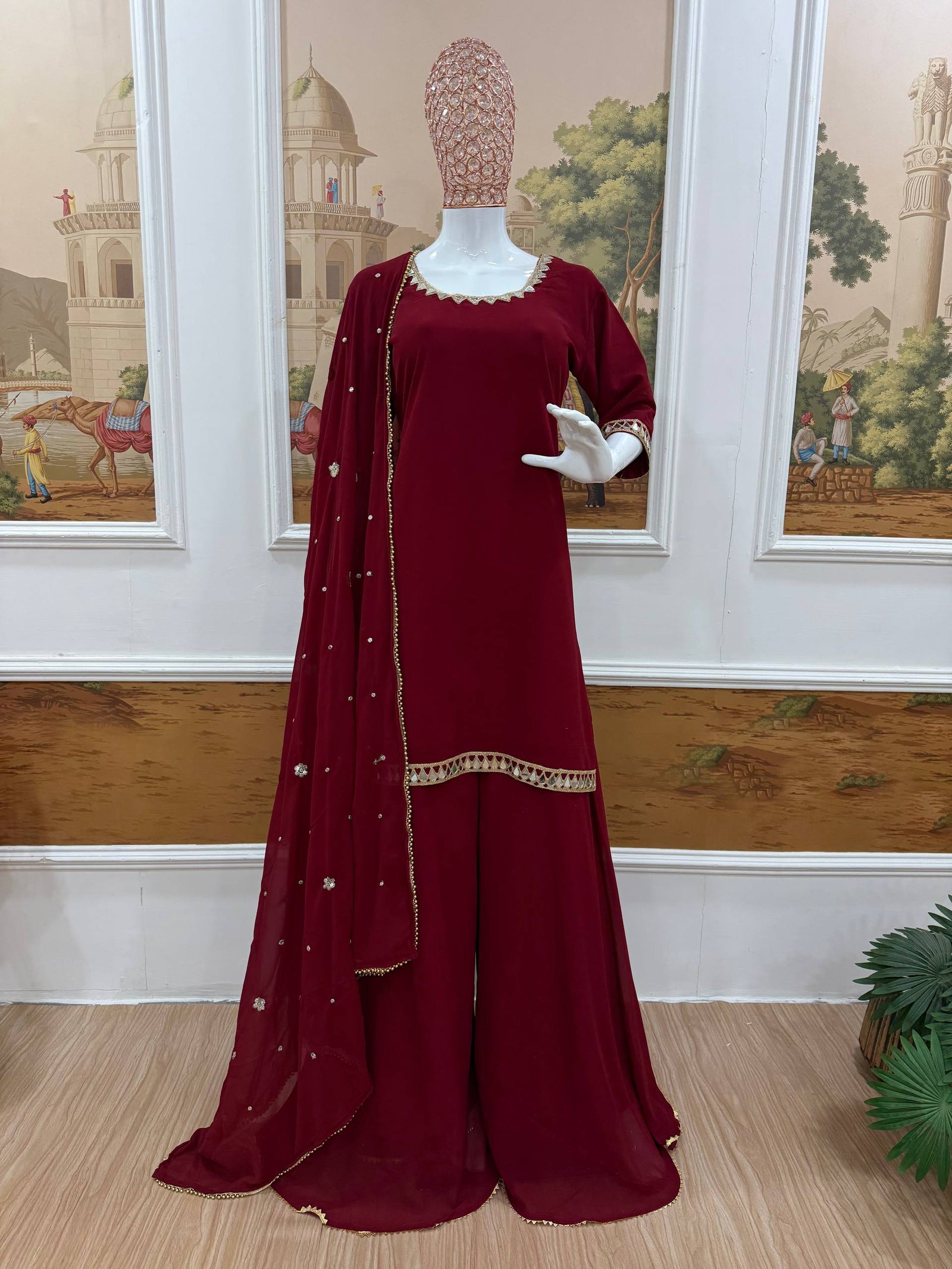 Maroon traditional outfit with a dupatta on a mannequin against a decorative wall.