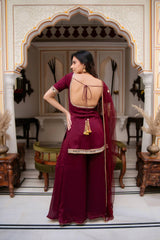 Woman in a burgundy saree with a decorative back design in an ornate room.