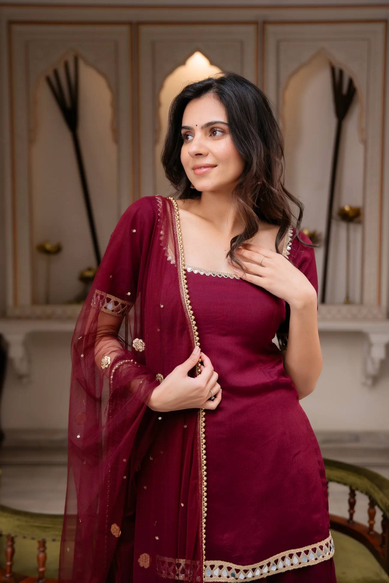 Woman in a maroon traditional outfit with a tiara in an elegant interior setting