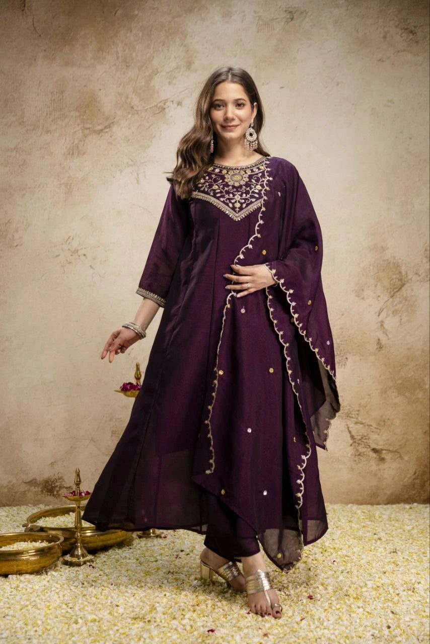 Woman wearing a purple traditional outfit with gold embroidery on a textured beige background