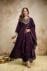 Woman wearing a purple traditional outfit with gold embroidery on a textured beige background