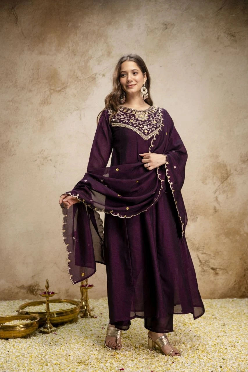 Woman in a traditional purple outfit with intricate designs against a textured beige background