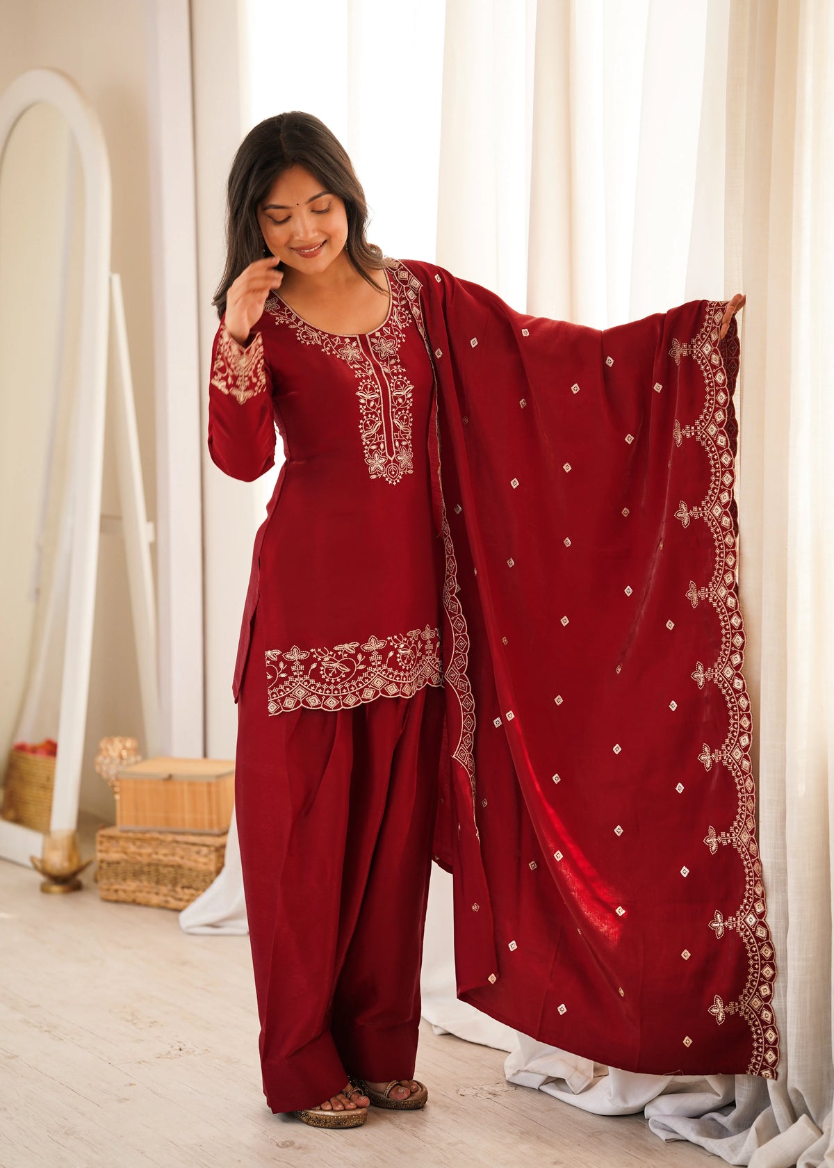 Woman in a red traditional outfit with white embroidery standing indoors.