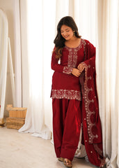Woman in a red traditional outfit with white embroidery standing in front of white curtains.