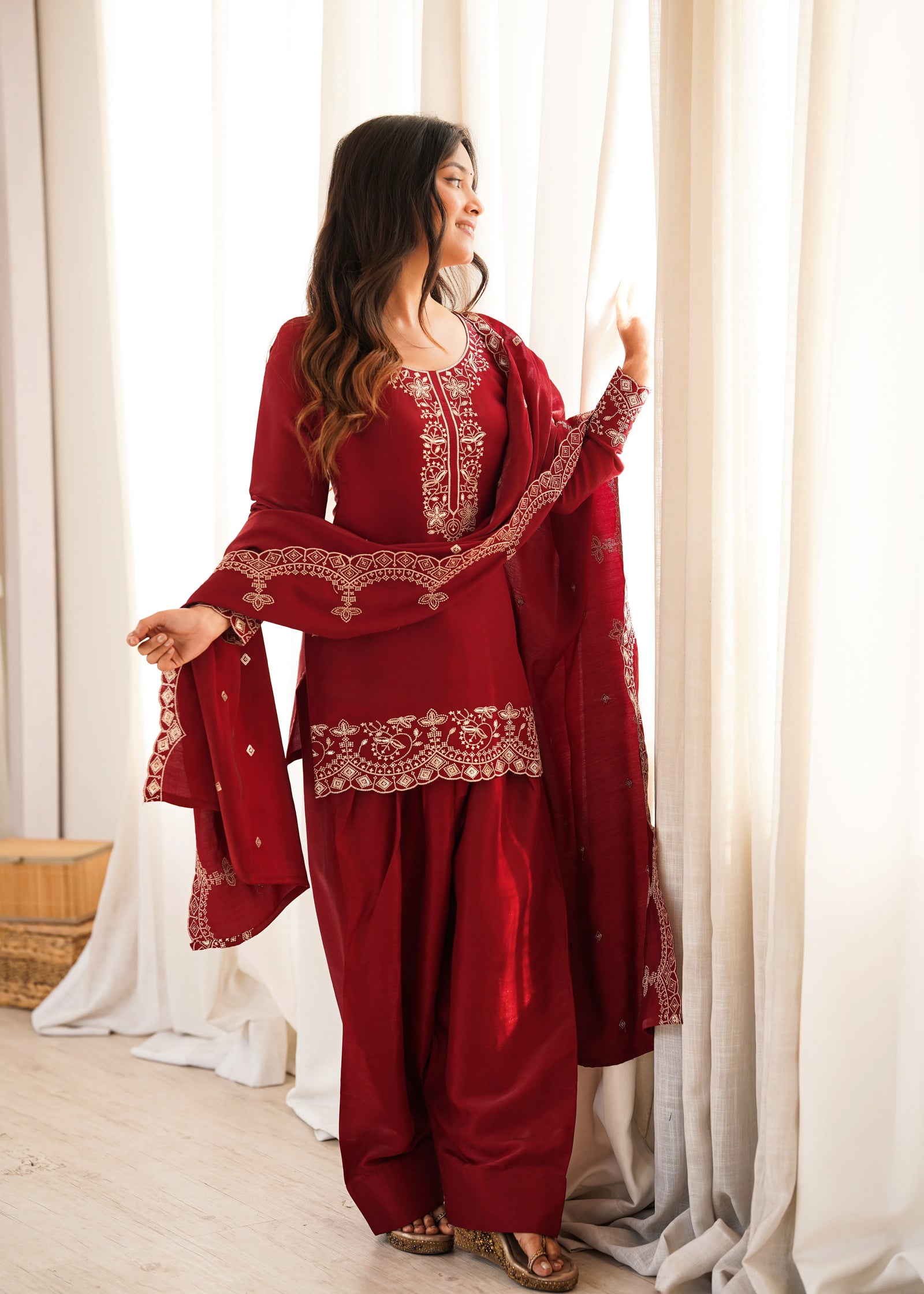 Woman wearing a red traditional outfit with intricate designs in a bright room.