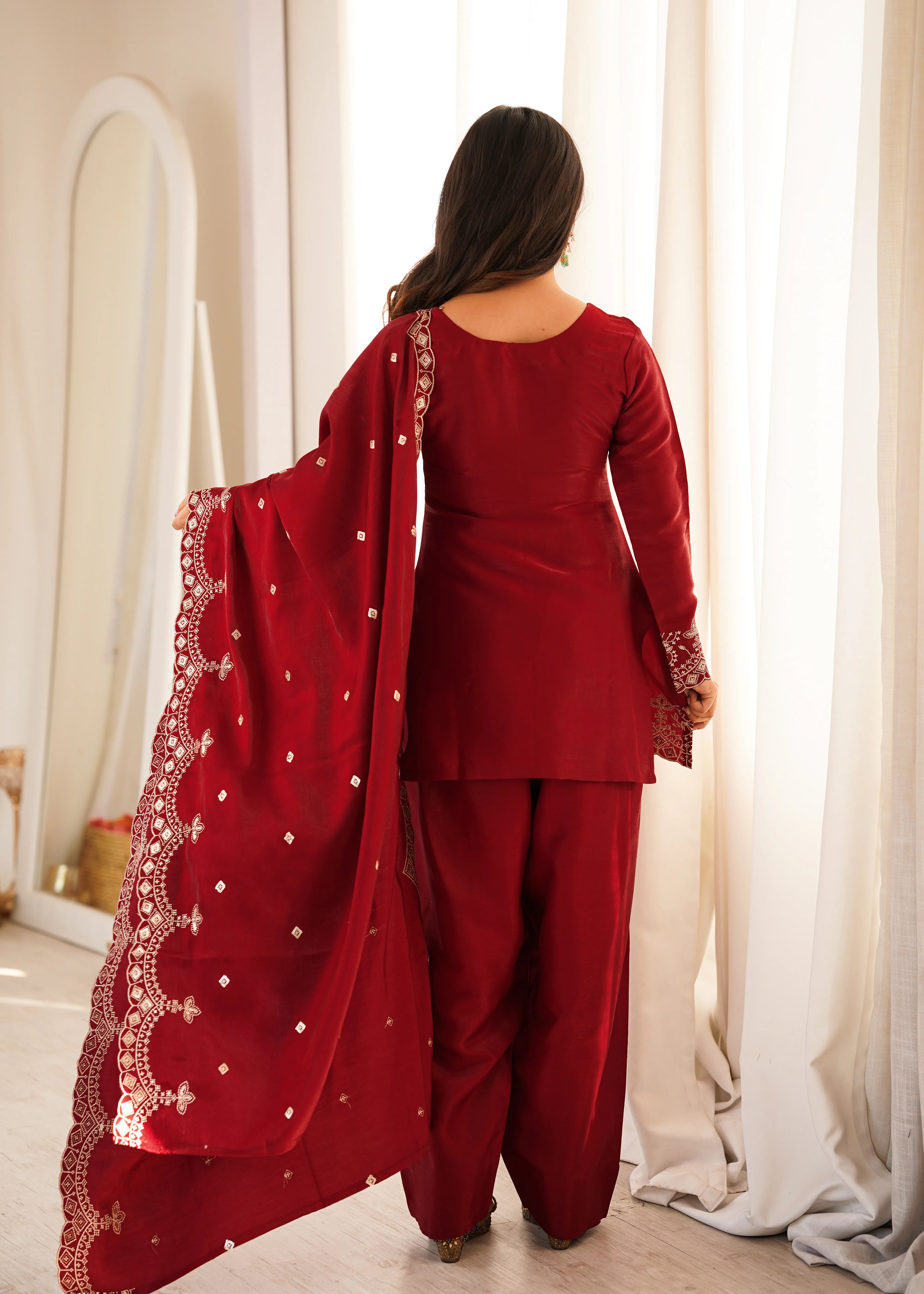 Woman in a red traditional outfit with a matching dupatta, standing in a well-lit room.