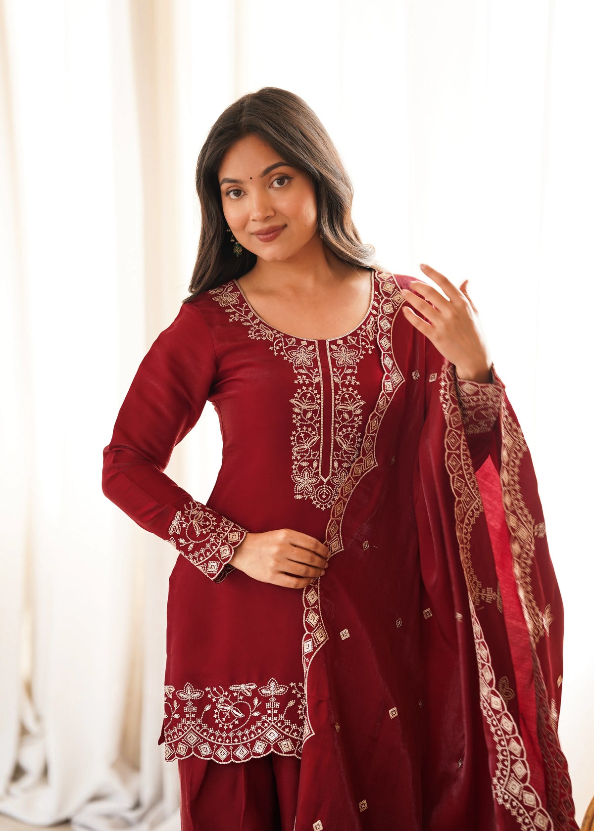 Woman wearing a maroon traditional outfit with intricate designs indoors.