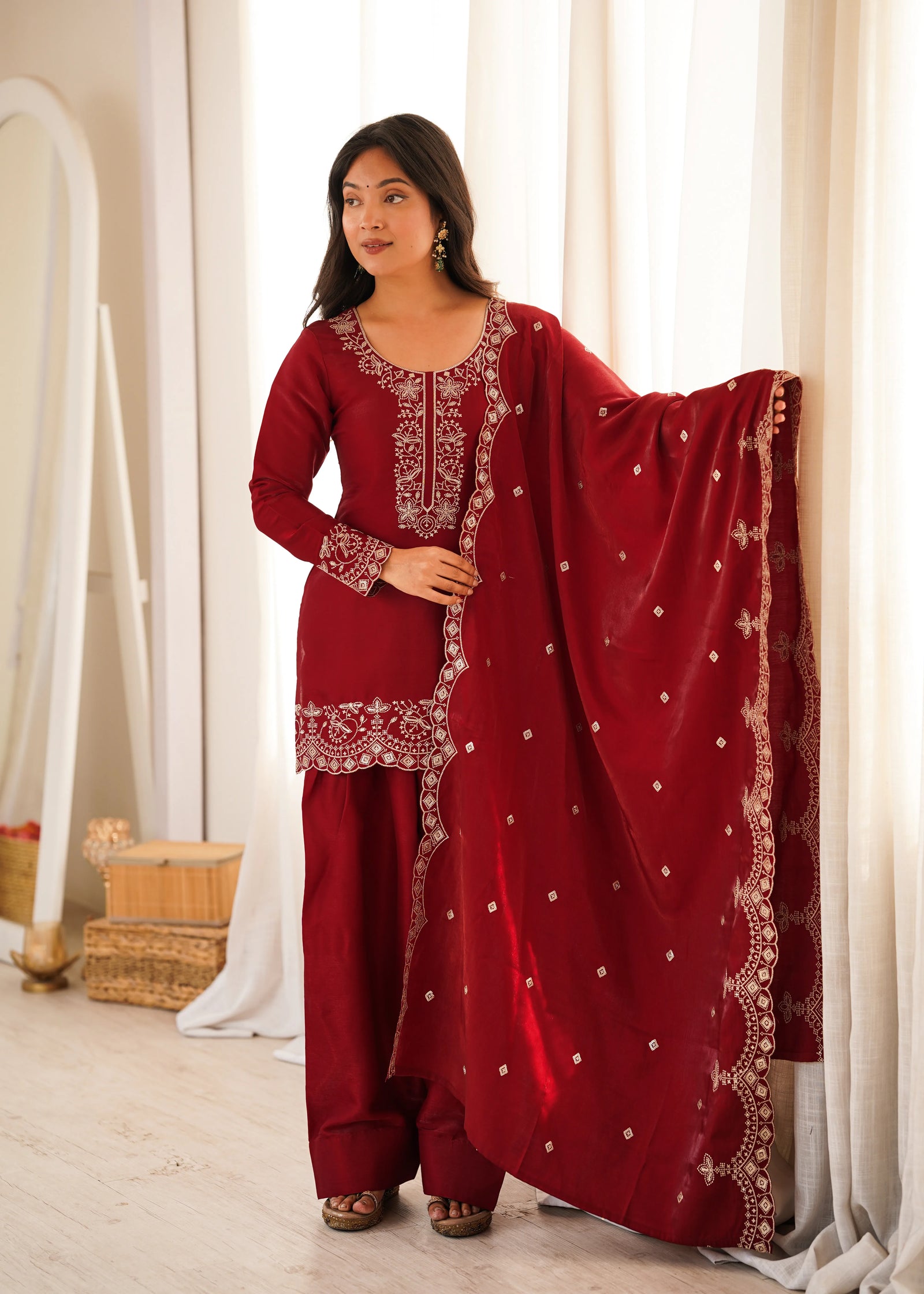 Woman wearing a red traditional outfit with white embroidery in a bright room.