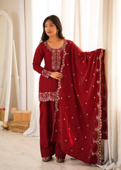 Woman wearing a red traditional outfit with white embroidery in a bright room.