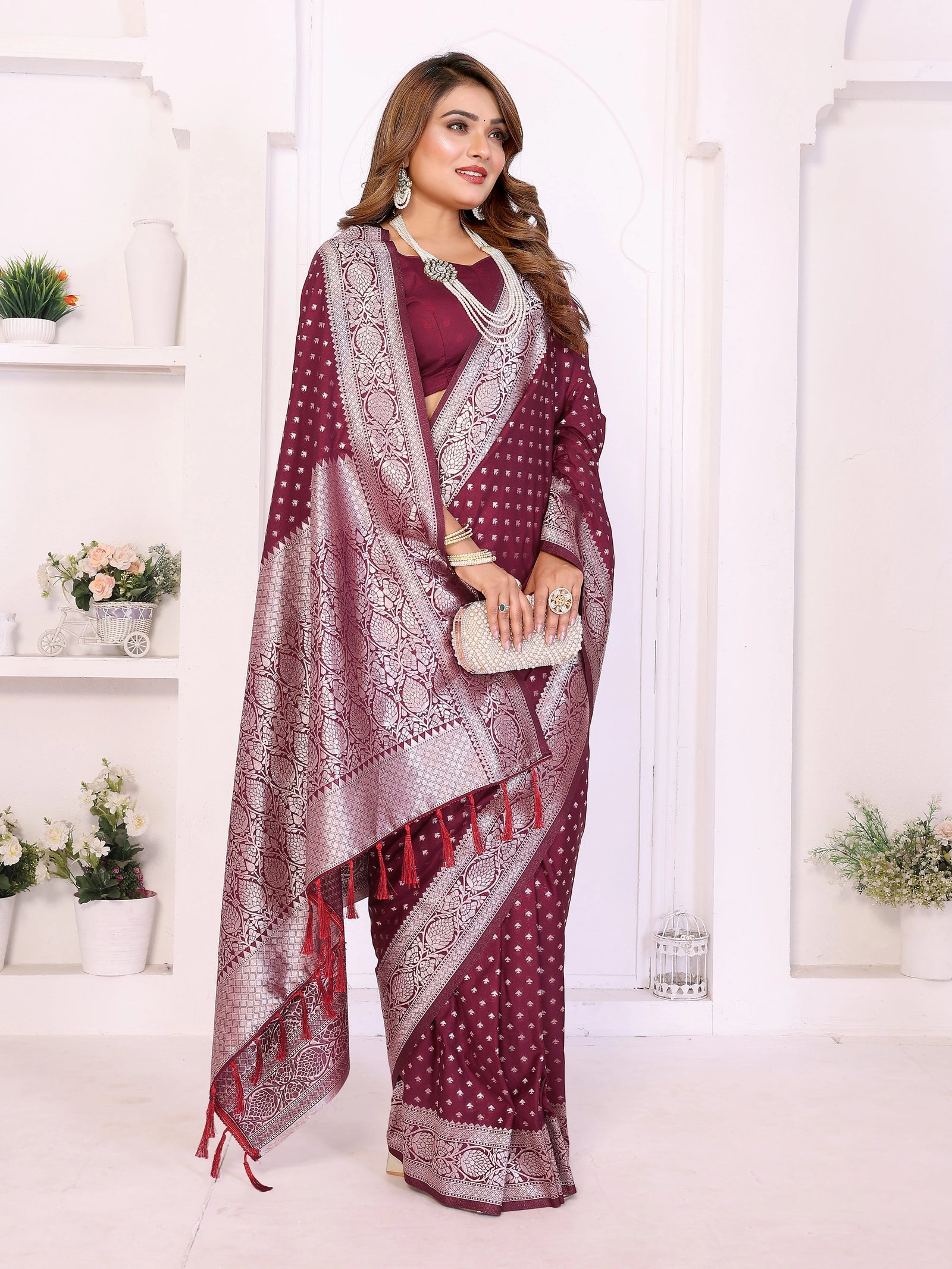 Woman wearing a maroon saree with white patterns in a white room.