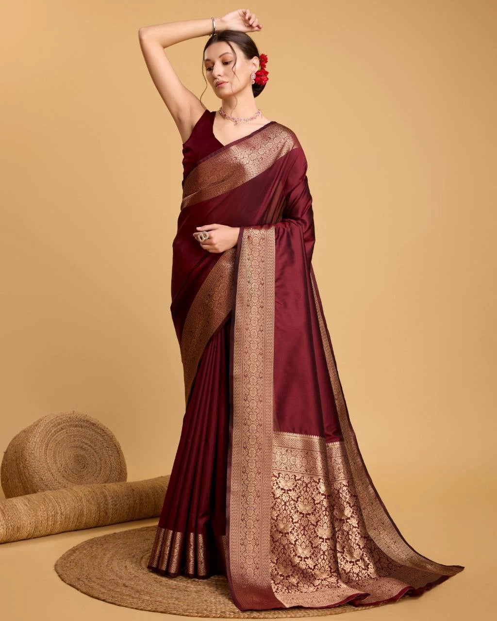 Woman wearing a maroon saree with gold border on a beige background