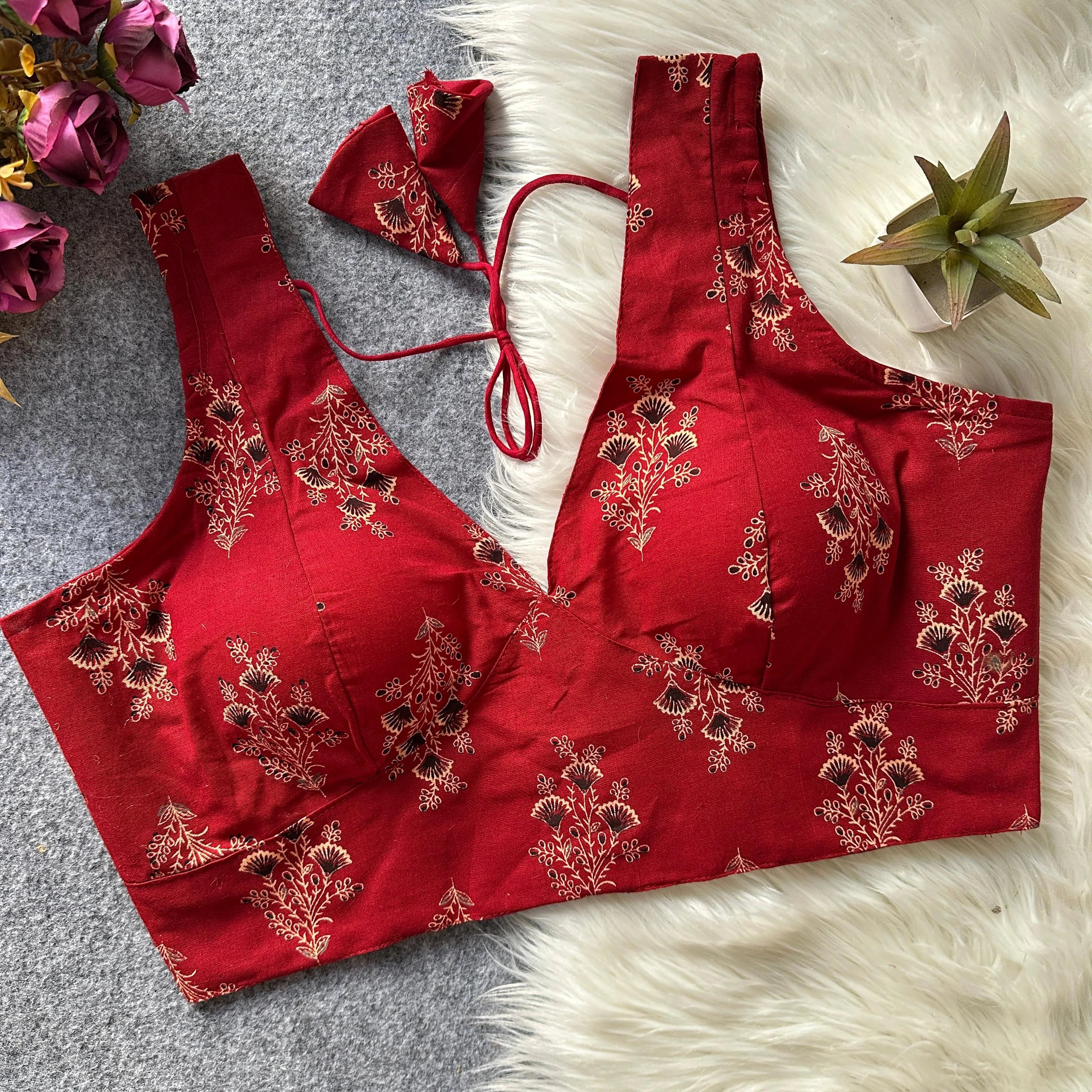 Red embroidered blouse on a textured surface with flowers and a plant.