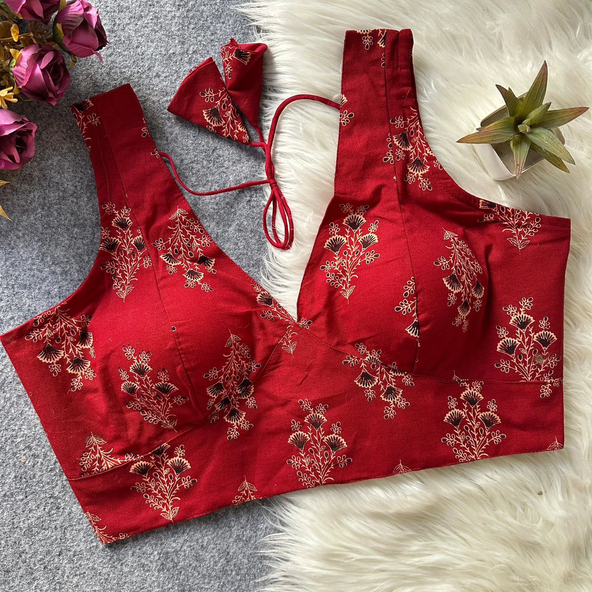 Red embroidered blouse on a textured surface with flowers and a plant.