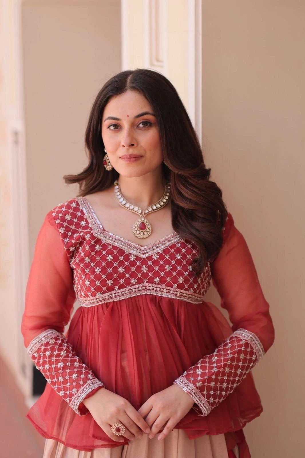 Woman wearing a red traditional outfit with intricate patterns and jewelry indoors.