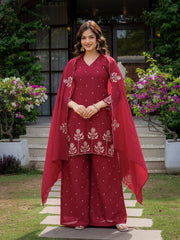 Woman in a red traditional outfit with floral patterns standing outdoors.