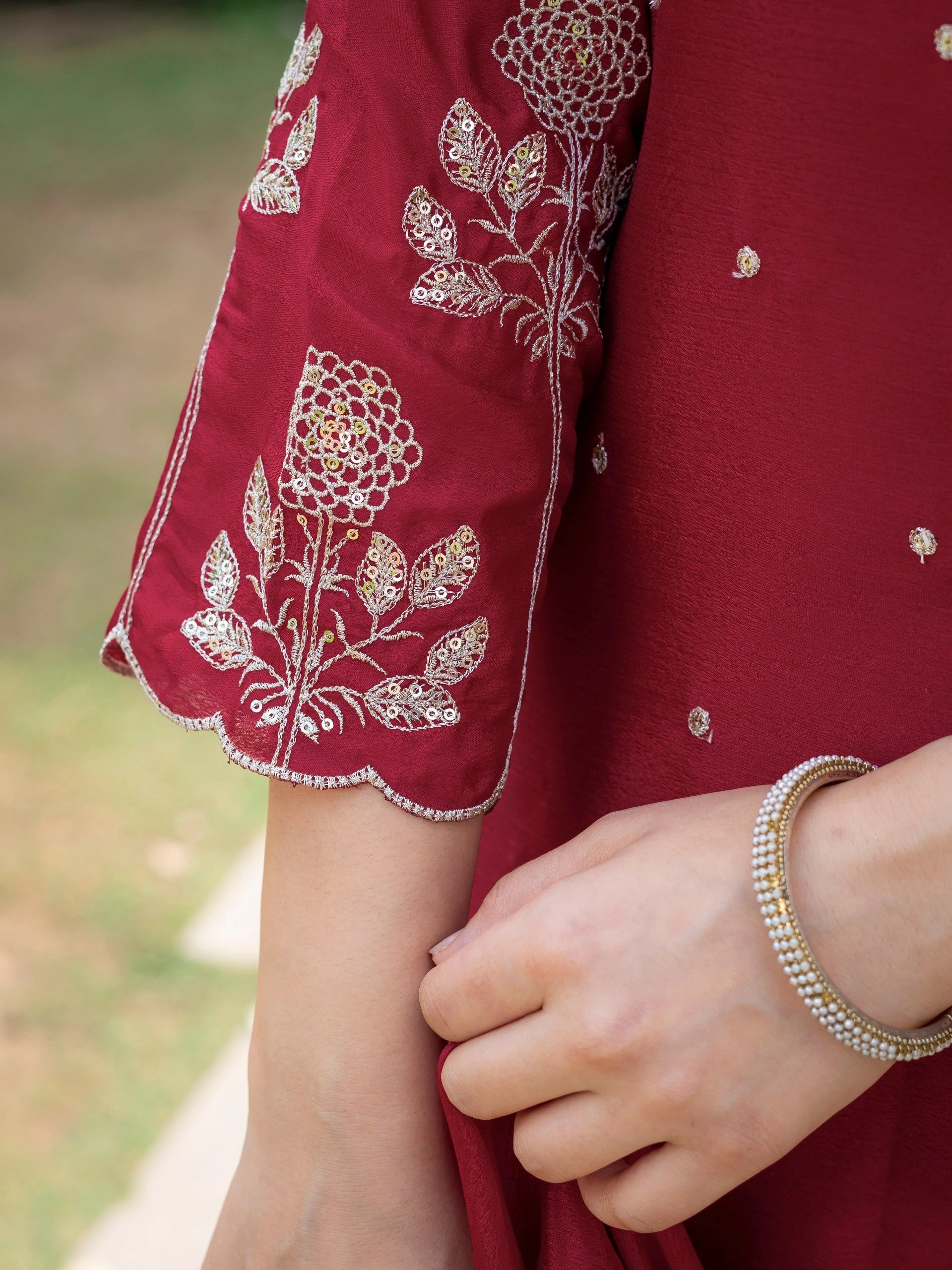 Close-up of a red garment with white floral embroidery and a hand wearing a bracelet.