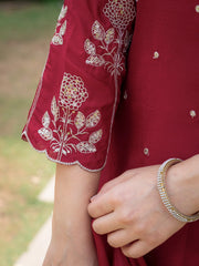 Close-up of a red garment with white floral embroidery and a hand wearing a bracelet.