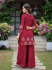 Woman in a maroon traditional outfit with white patterns standing outdoors.