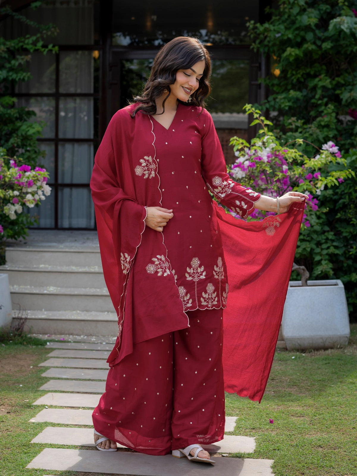 Woman in a red traditional outfit with floral patterns standing outdoors.