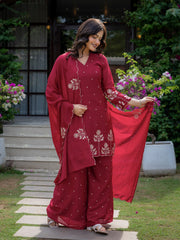 Woman in a red traditional outfit with floral patterns standing outdoors.