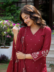 Woman wearing a red traditional outfit with floral patterns in an outdoor setting.