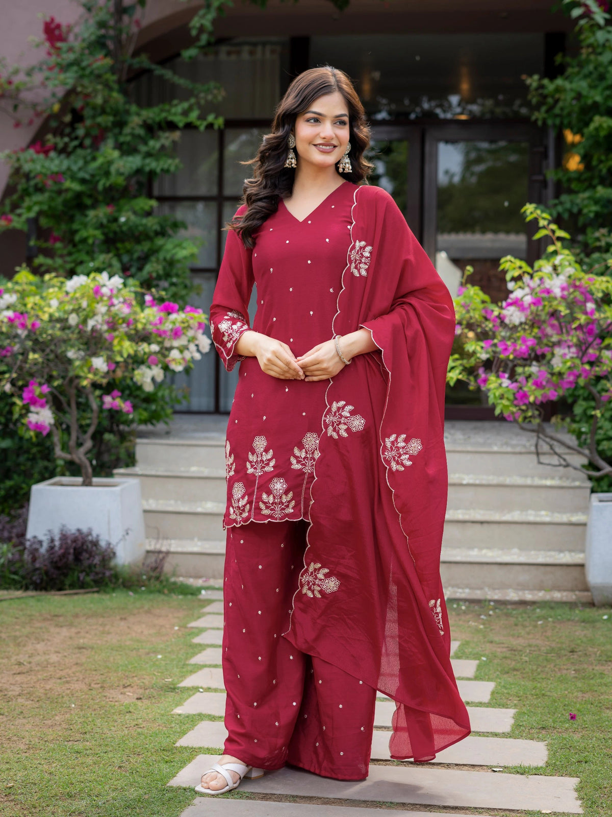 Woman in a red traditional outfit standing outdoors with greenery in the background
