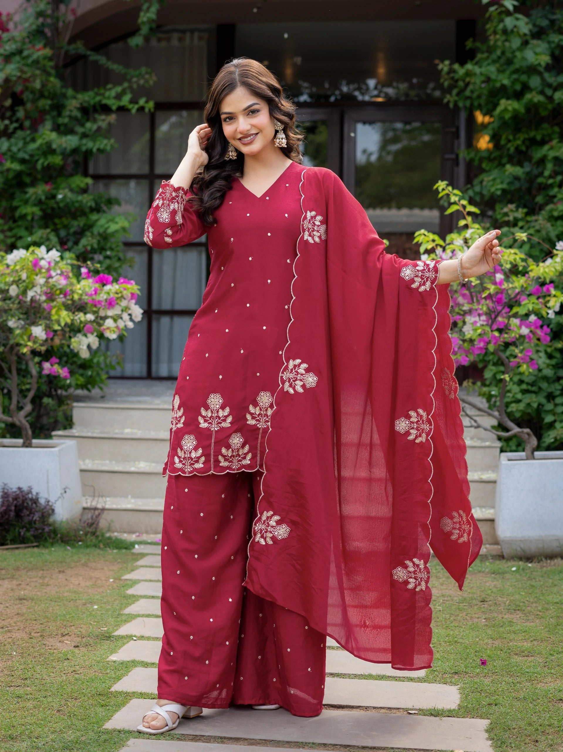 Woman in a red traditional outfit with floral patterns standing outdoors.