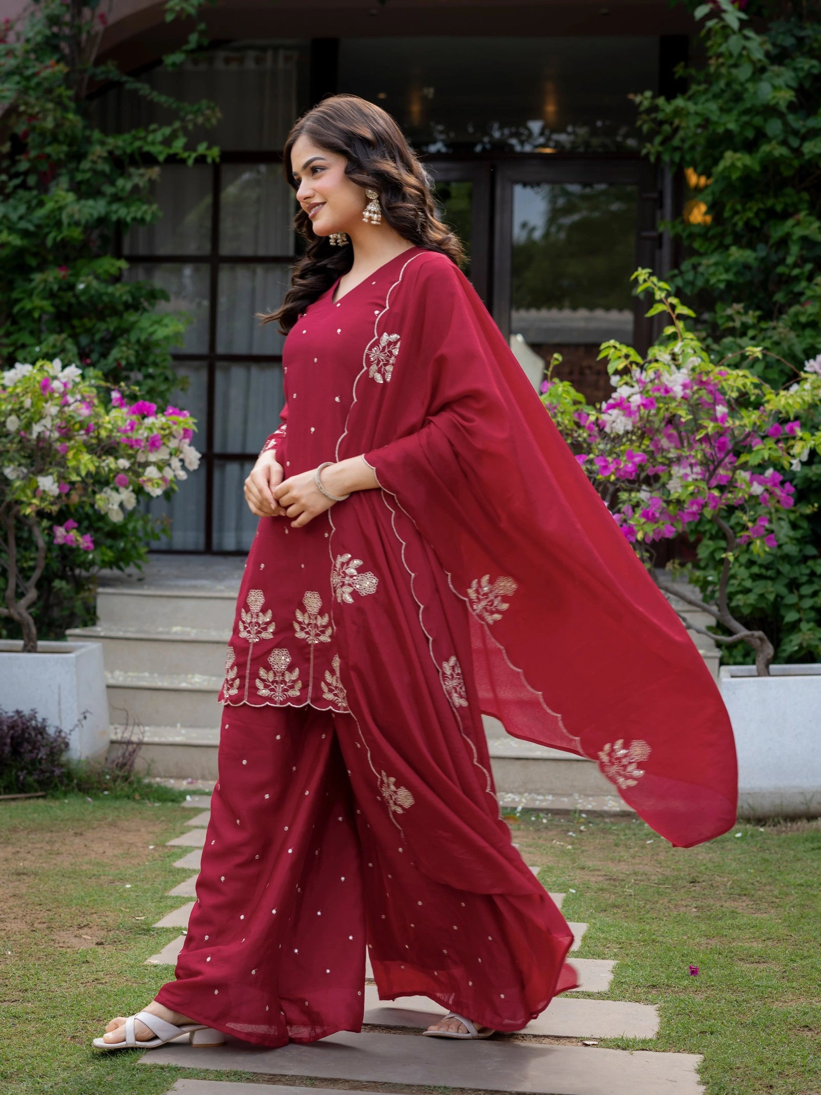 Woman in a red traditional outfit with floral patterns standing outdoors.