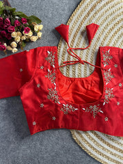 A vibrant red raw silk blouse featuring a deep U-shaped back. The neckline is adorned with delicate hand-embroidered floral sprigs in white and gold thread. Matching red tie-back tassels are attached at the shoulders, and the rest of the back is sprinkled with small embroidered floral motifs.