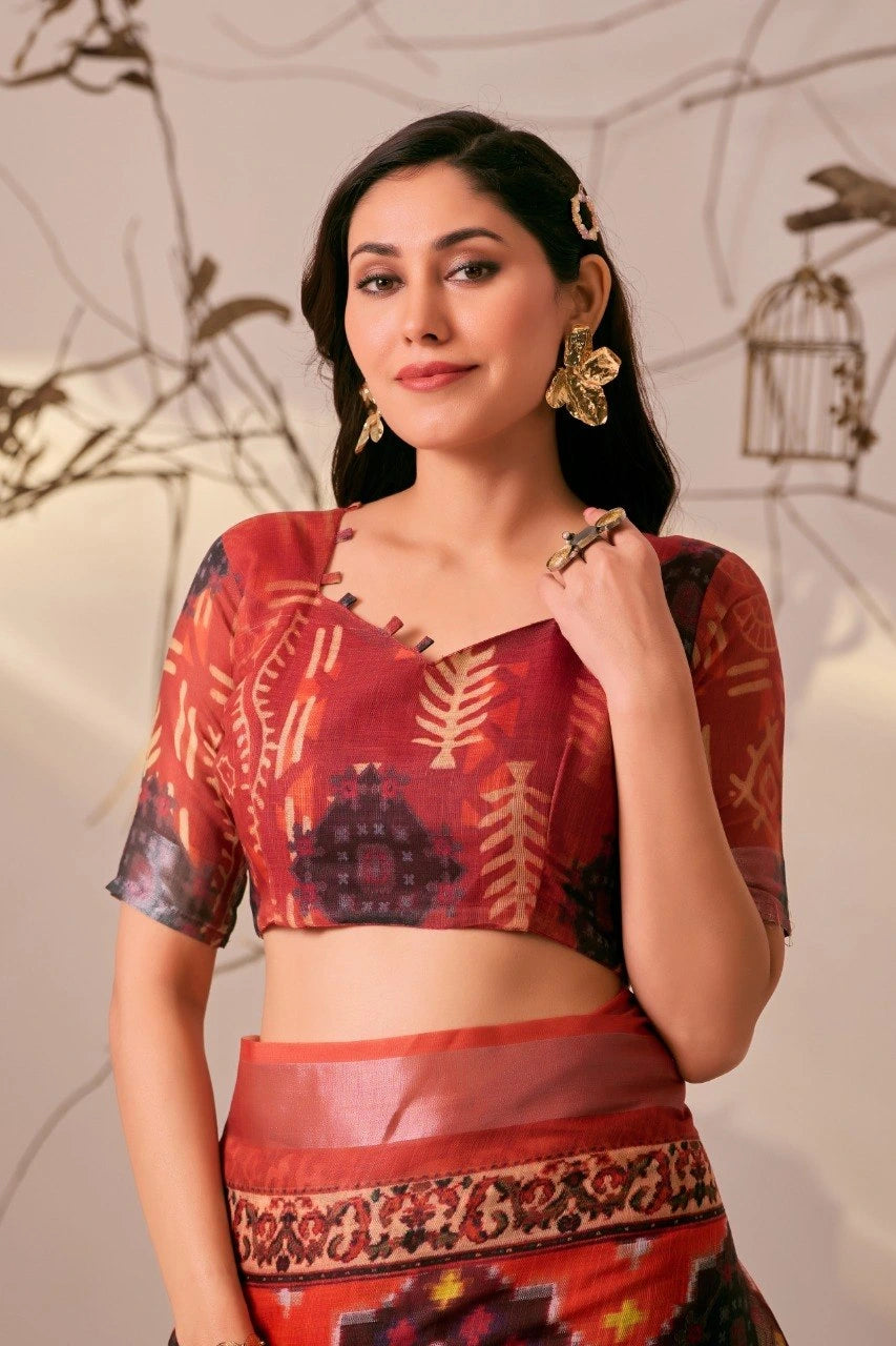 Woman wearing a traditional red and black patterned outfit with gold jewelry against a neutral background.