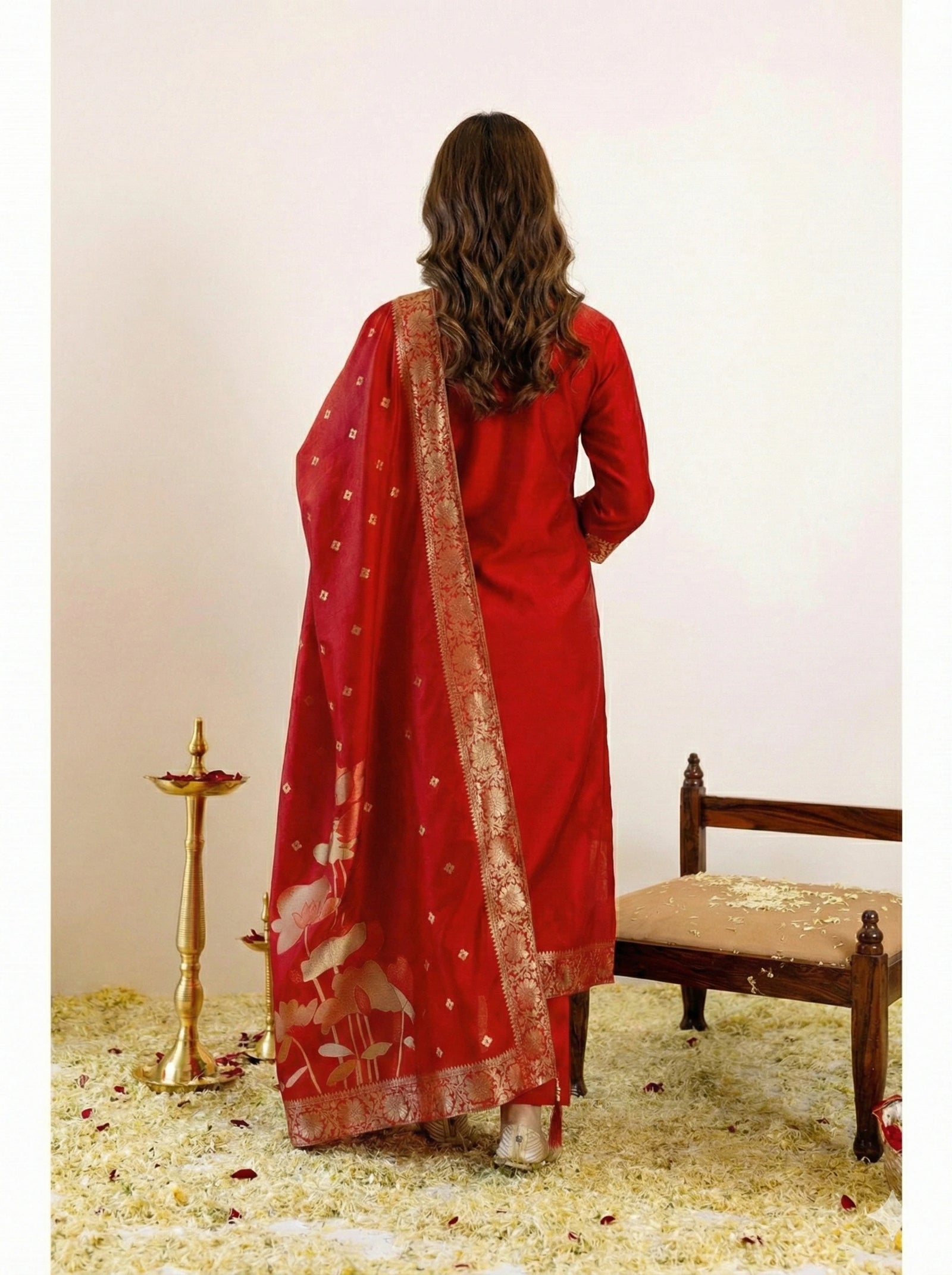 Woman wearing a red traditional outfit with a matching dupatta, standing in a decorated room.