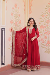 Woman in a red traditional outfit with gold embroidery against a decorative wall.