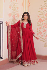 Woman in a red traditional outfit with gold embroidery against a floral wall.