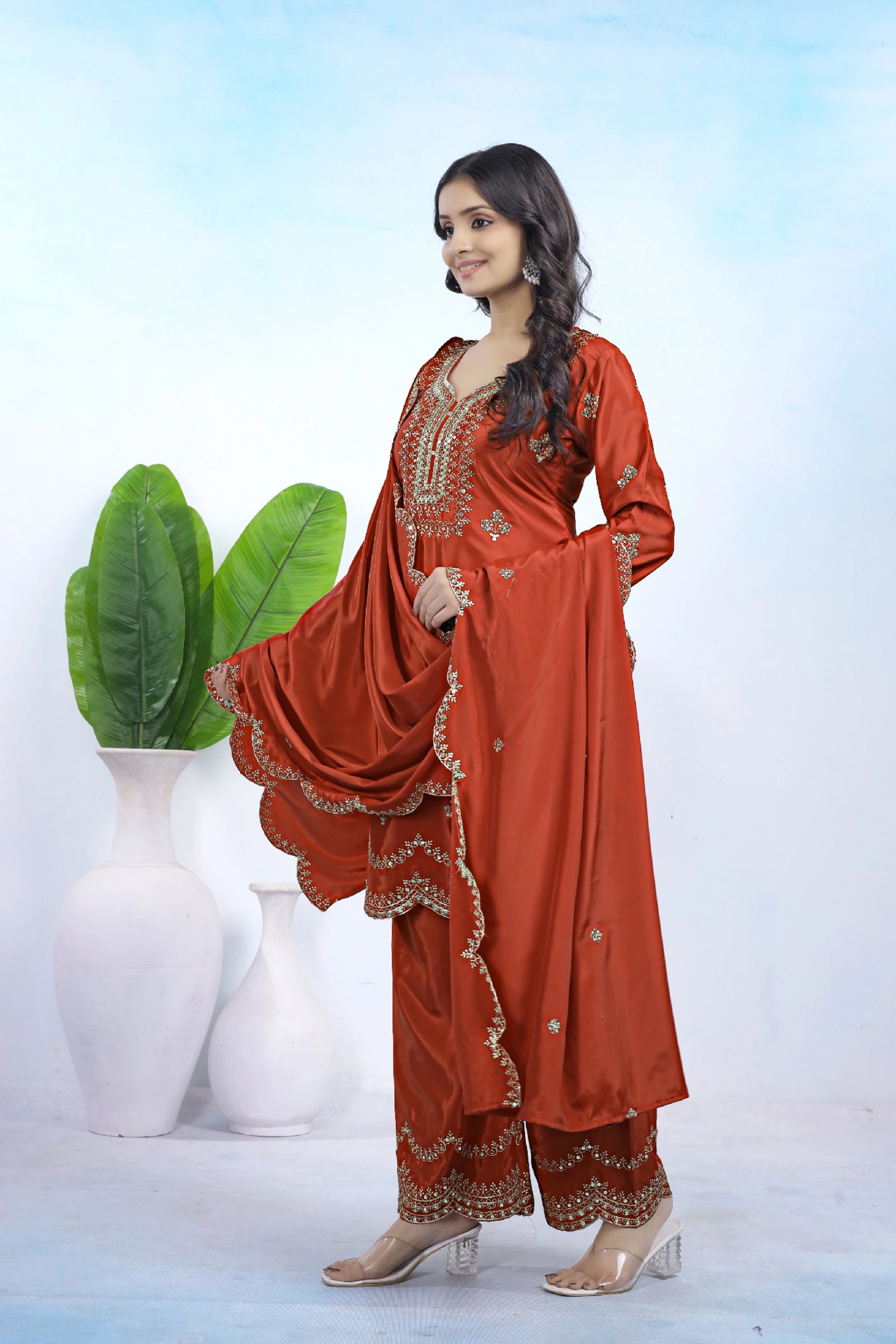 Woman wearing a traditional red outfit with intricate designs, standing against a light blue background.