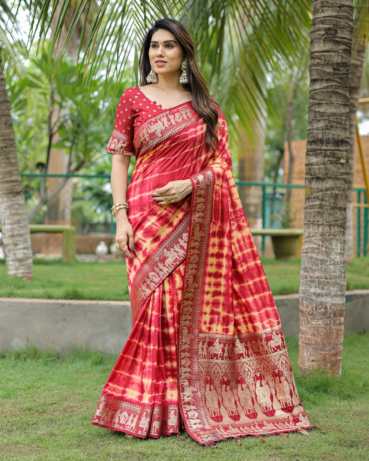 Woman wearing a red and yellow saree with elephant patterns in a garden setting