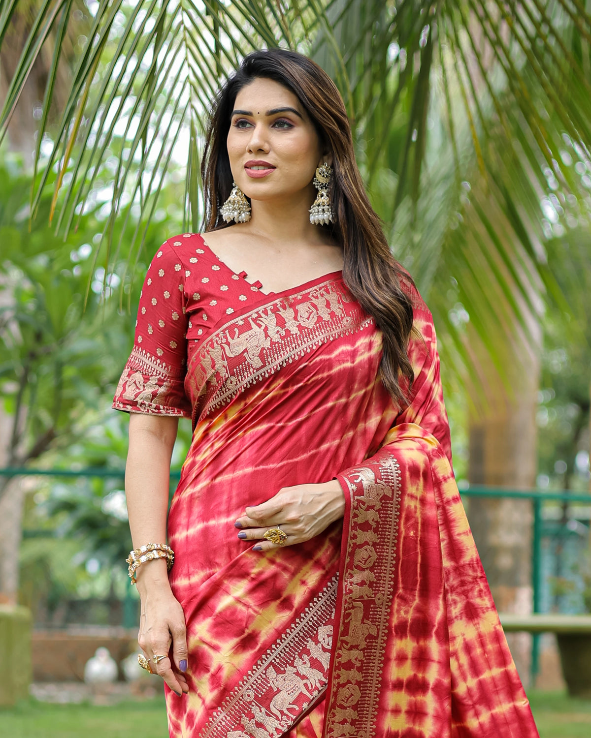Woman wearing a red and gold saree with a tropical background