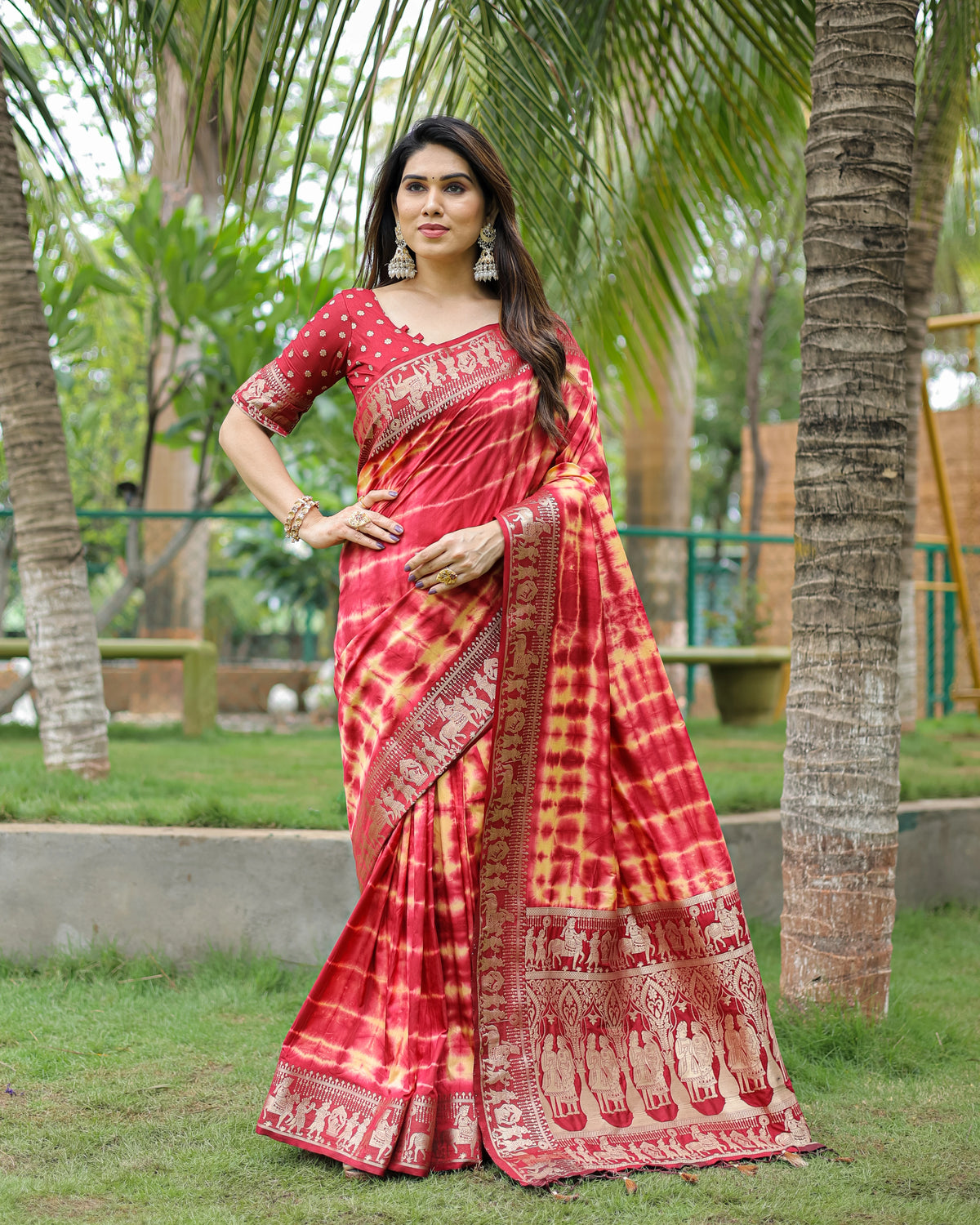 Woman in a red and yellow saree standing outdoors with trees in the background