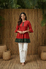 Woman wearing a red and green top with white pants standing against a wooden wall.