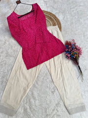 Pink embroidered top and beige pants on a textured surface with flowers.