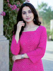 Woman wearing a pink traditional outfit with floral patterns outdoors.