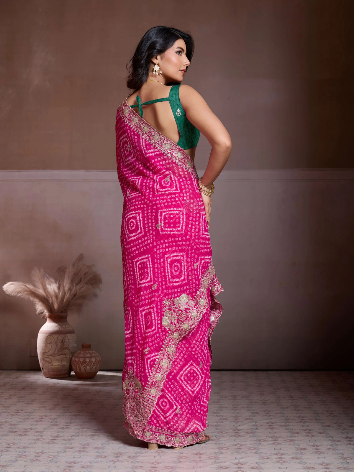 Woman wearing a pink saree with a green blouse against a brown background